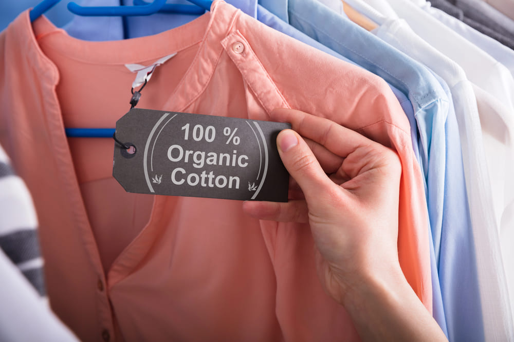 abbigliamento eco-friendly autunno 2024: camicia in cotone organico al 100% con cartellino, tra una selezione di capi sostenibili appesi su grucce