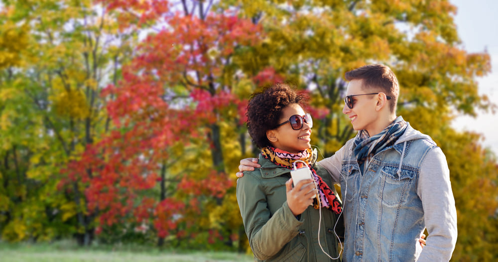 Coppia che indossa occhiali da sole durante una passeggiata autunnale in un parco, circondati dai colori tipici dell'autunno.